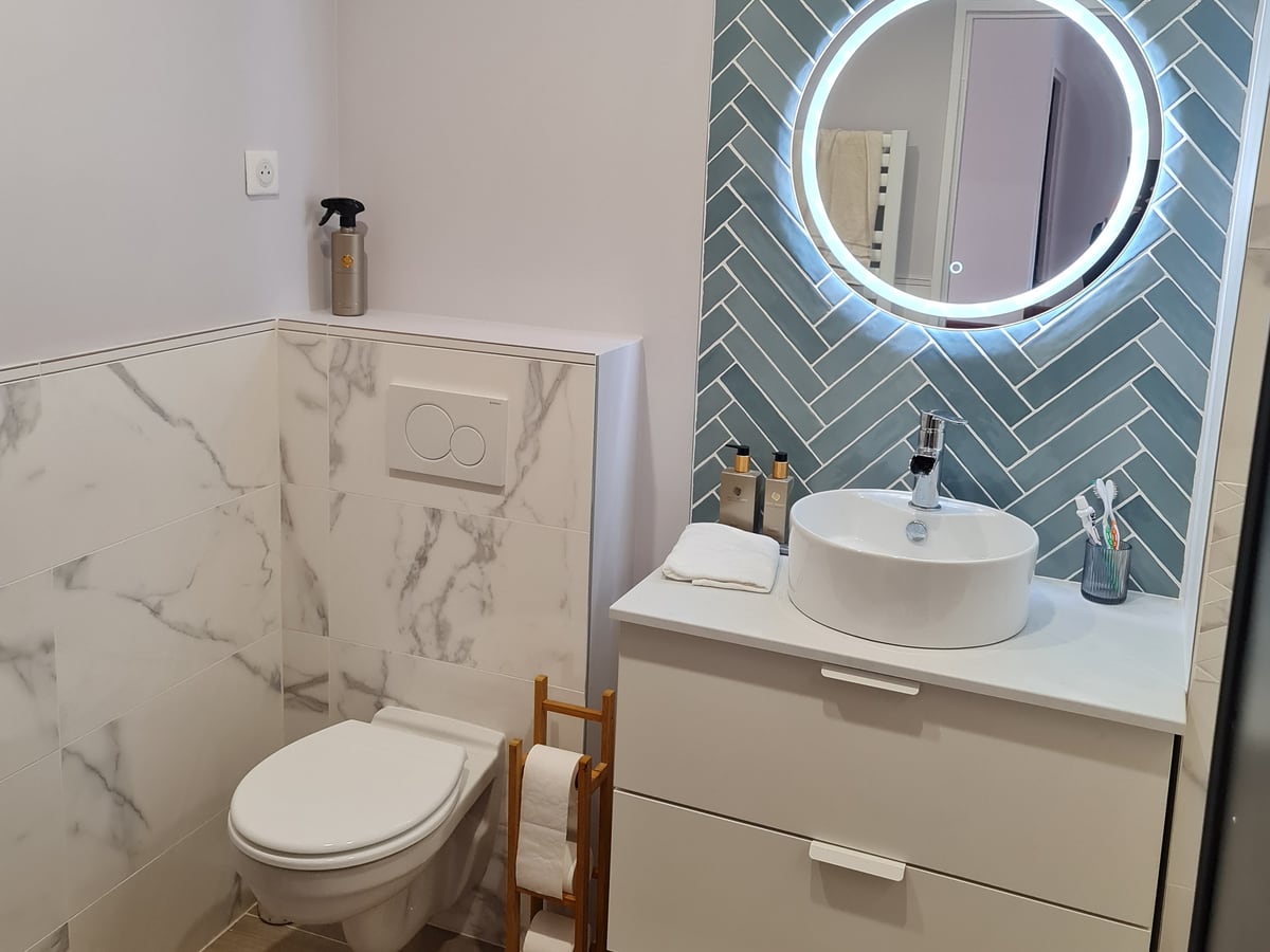 Salle d'eau terminée avec faïence bleue en chevrons, vasque ronde et miroir rétroéclairé