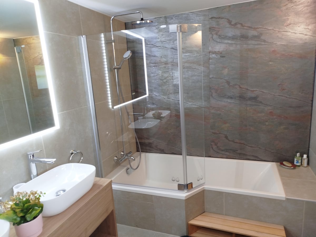 Salle de bains rénovée avec baignoire, colonne de douche et mur en pierre naturelle